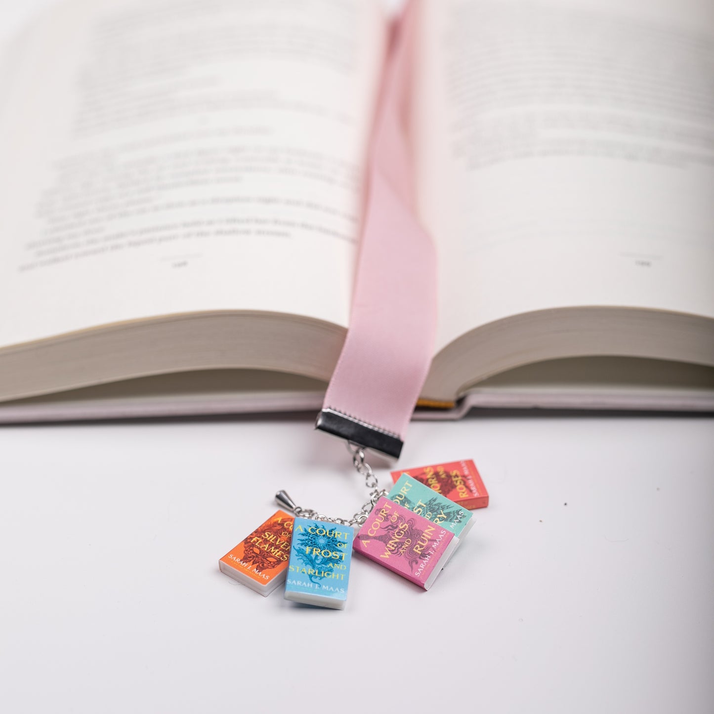 Pink, velvet bookmark with ACOTAR mini book charms marking the page in an open book