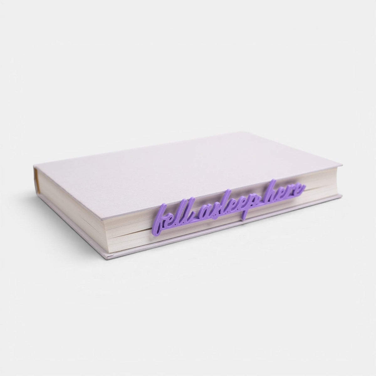 The Salty Cat Co purple Fell Asleep Here bookmark inserted into a closed book on a white background.