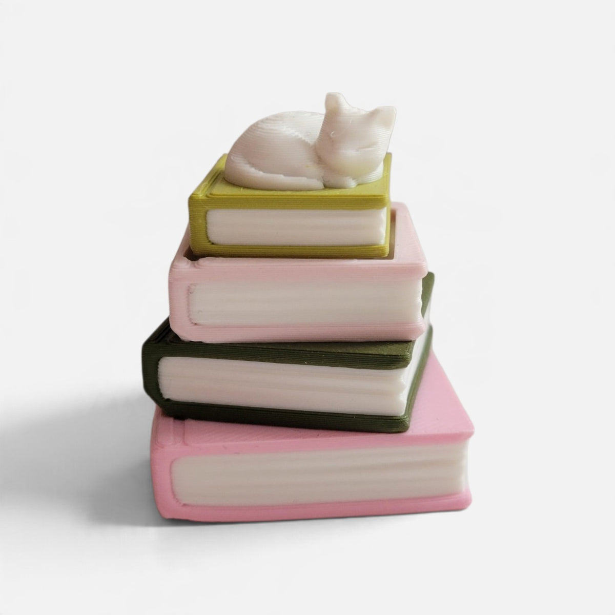 A small decorative figurine shaped like a stack of four books with a white cat curled up sleeping on top, photographed on a clean white background.