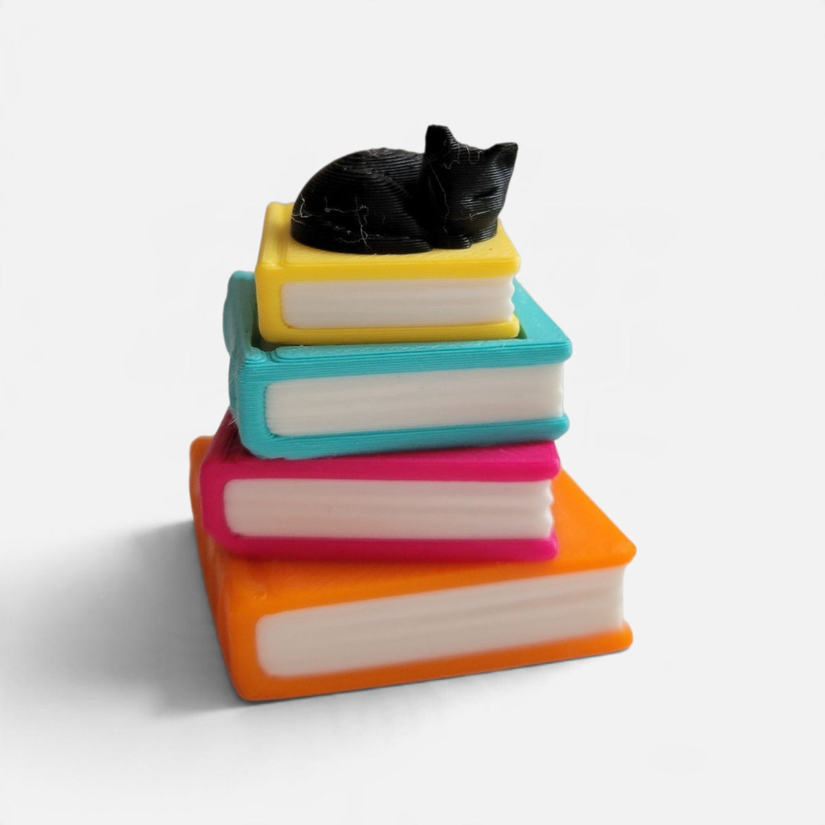 A small decorative figurine of a black cat sleeping on top of a stack of four colorful books in yellow, turquoise, pink, and orange, set against a plain white background.