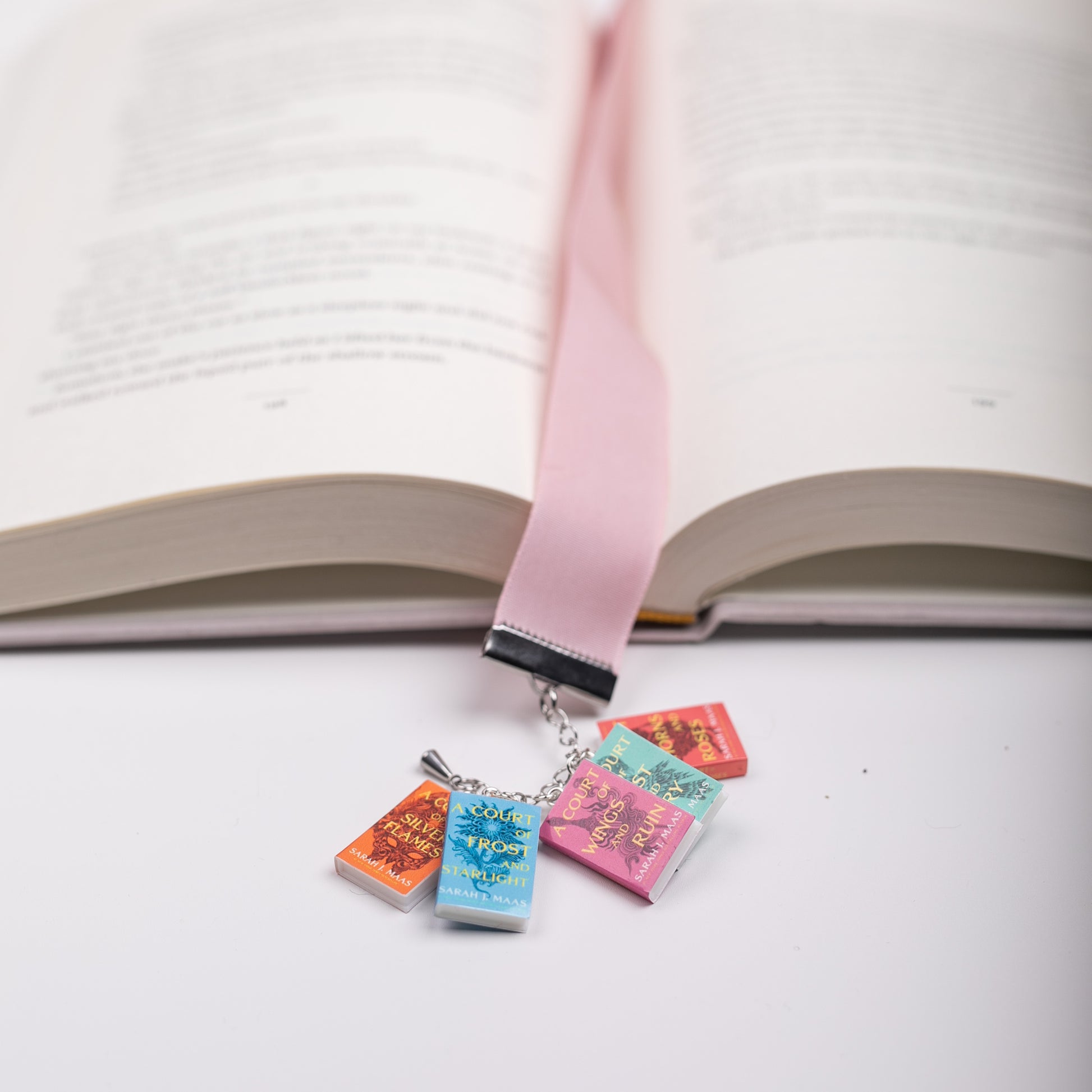 Pink, velvet bookmark with ACOTAR mini book charms marking the page in an open book
