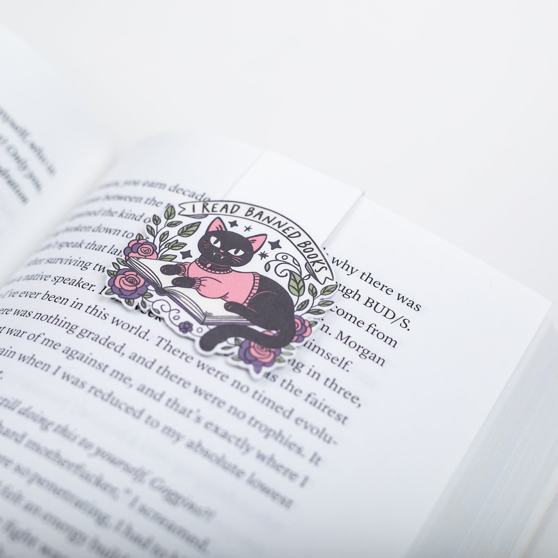 Bookmark of a black cat in a pink sweater with floral elements on a book.