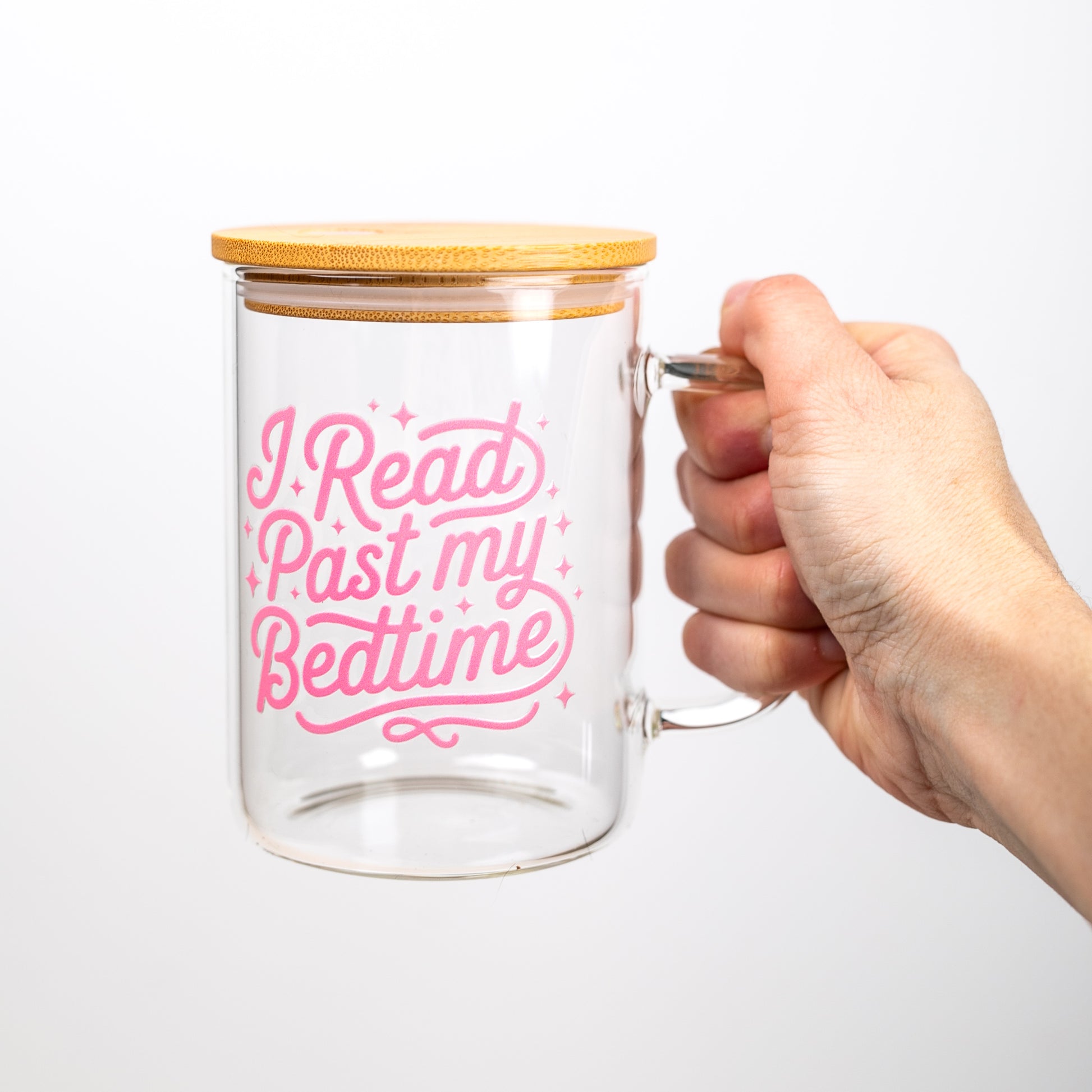 Glass mug with bamboo lid held by a hand, featuring pink text on a white background
