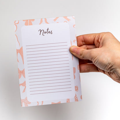 Hand holding a small notepad with 'Notes' text and pink bow design on a white background