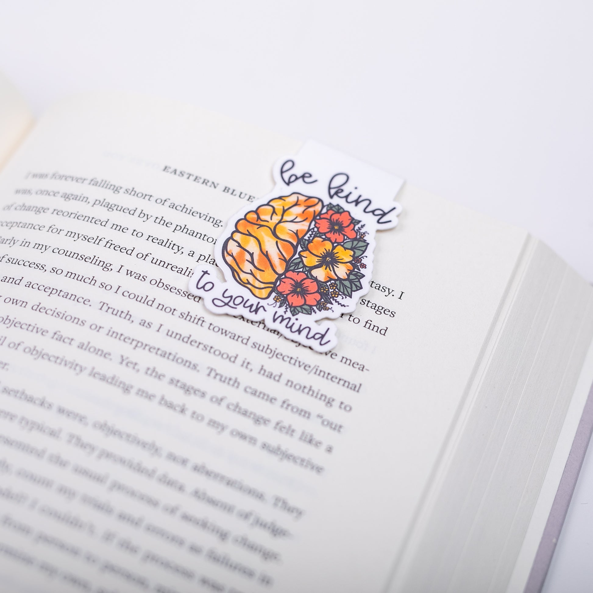 Open book with a decorative bookmark featuring brain and flowers design and text on a white background