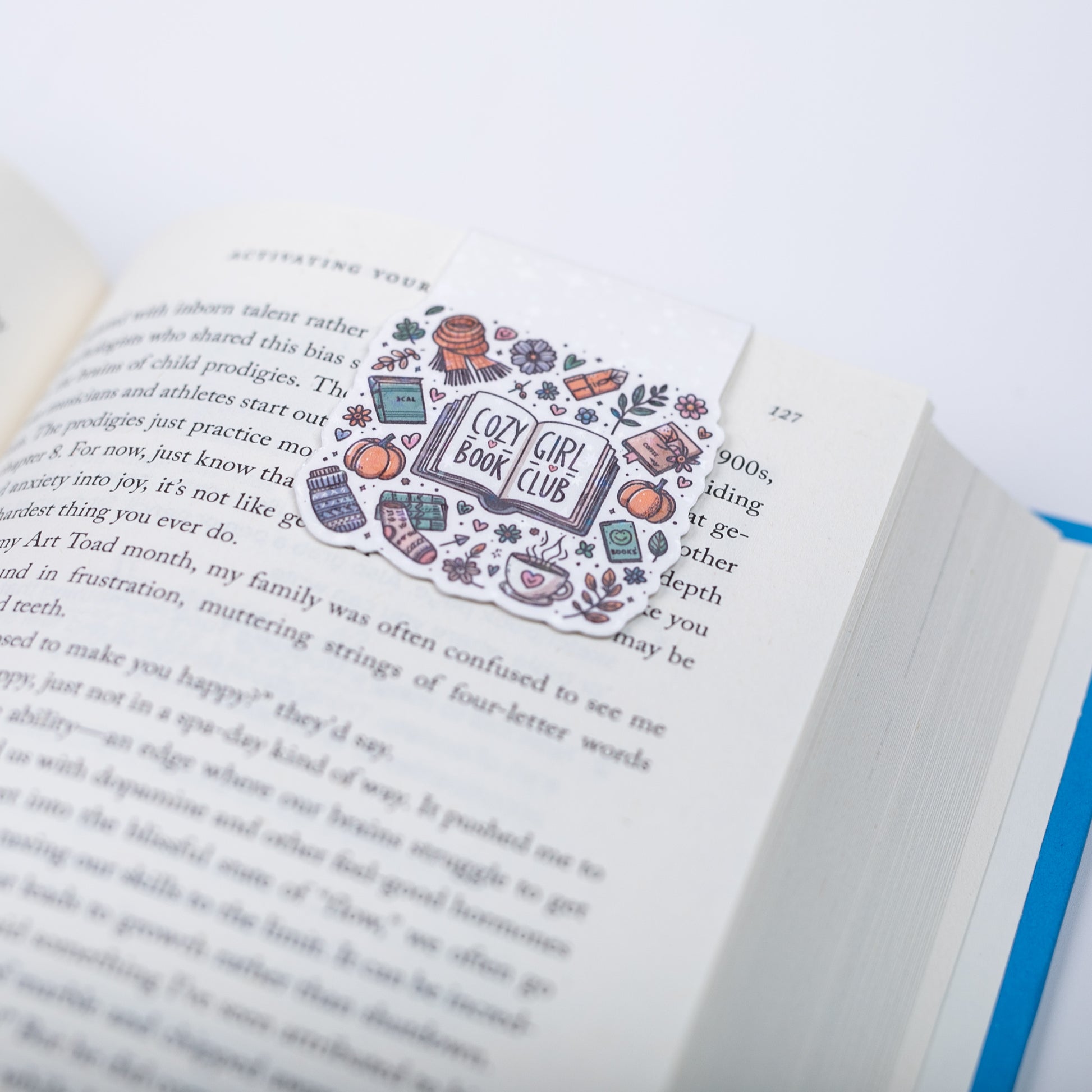 Open book with a magnetic bookmark featuring 'Cozy Girl Book Club' design on a white background