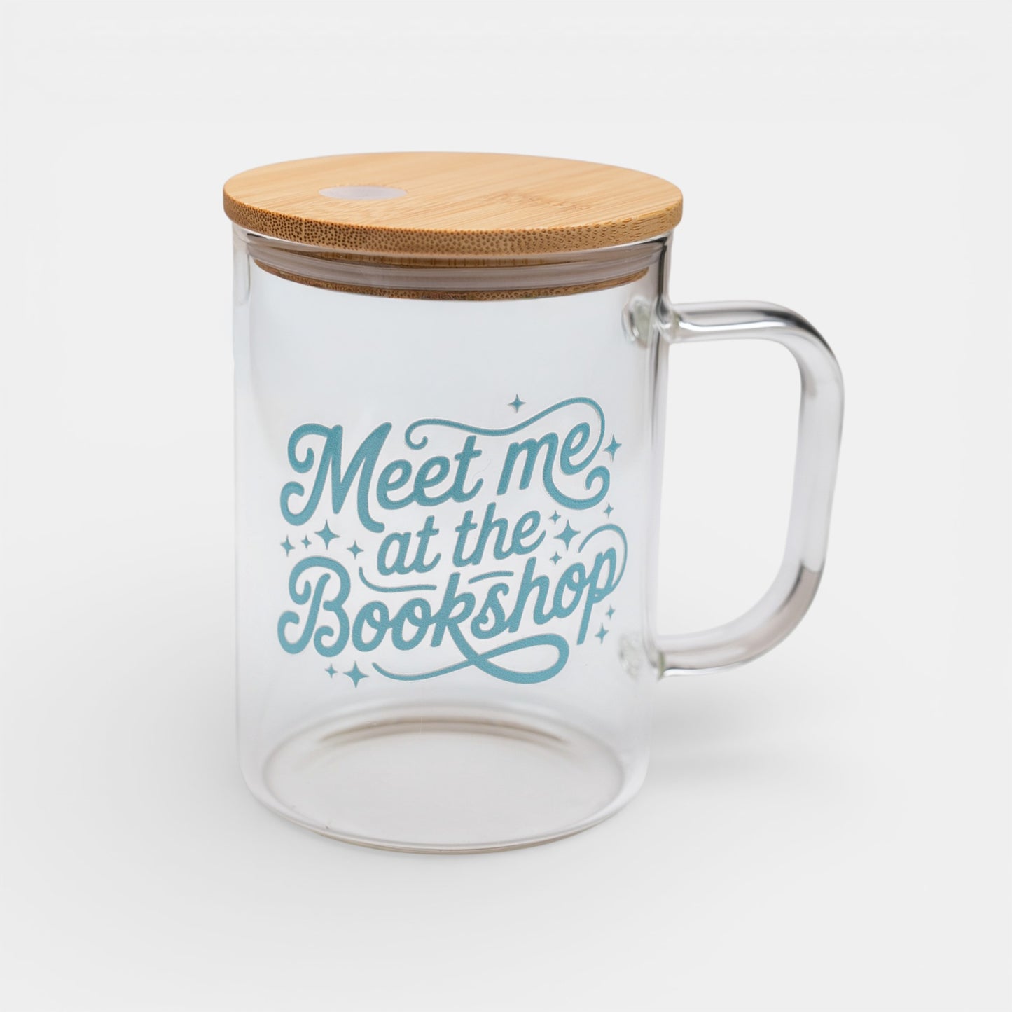 Clear glass mug with bamboo lid and 'Meet me at the Bookshop' text on a white background
