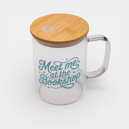 Clear glass mug with bamboo lid and 'Meet me at the Bookshop' text on a white background