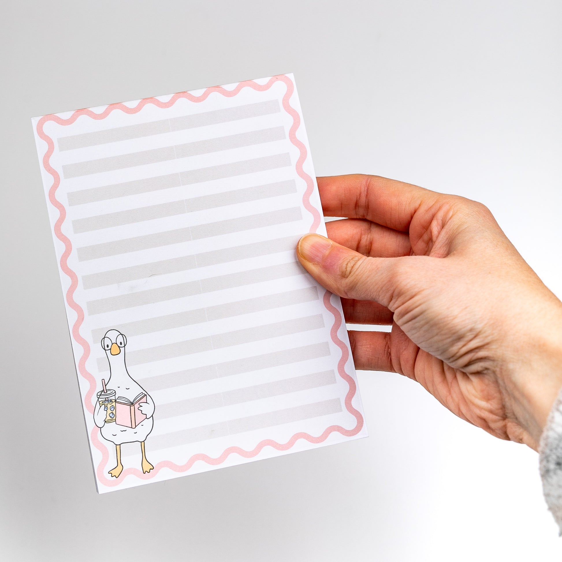 Hand holding a notepad with a cartoon duck design on a gray background