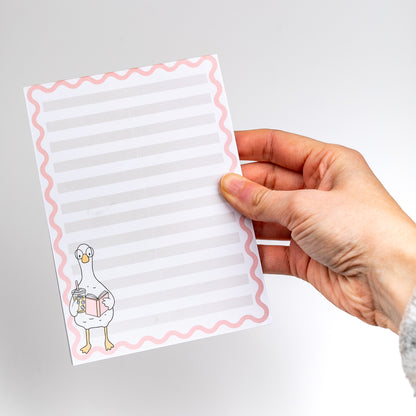 Hand holding a notepad with a cartoon duck design on a gray background