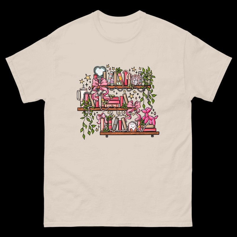 The Salty Cat Co sand-colored crewneck t-shirt featuring a whimsical bookshelf graphic with pink bows and greenery.