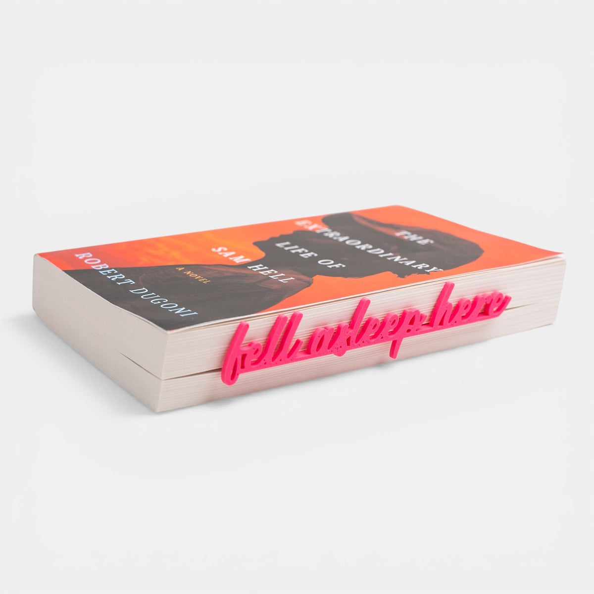 The Salty Cat Co Fell Asleep Here bookmark in bright pink, inserted into a paperback book on a white background.