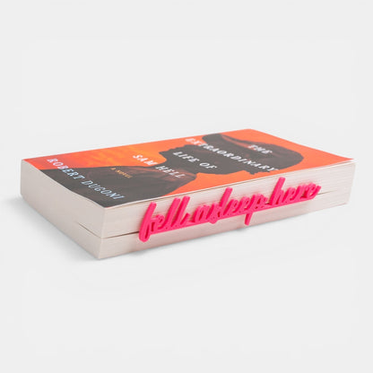 The Salty Cat Co pink Fell Asleep Here script bookmark clipped onto the edge of a paperback book