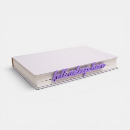 The Salty Cat Co purple Fell Asleep Here bookmark placed inside a closed book on a white background.