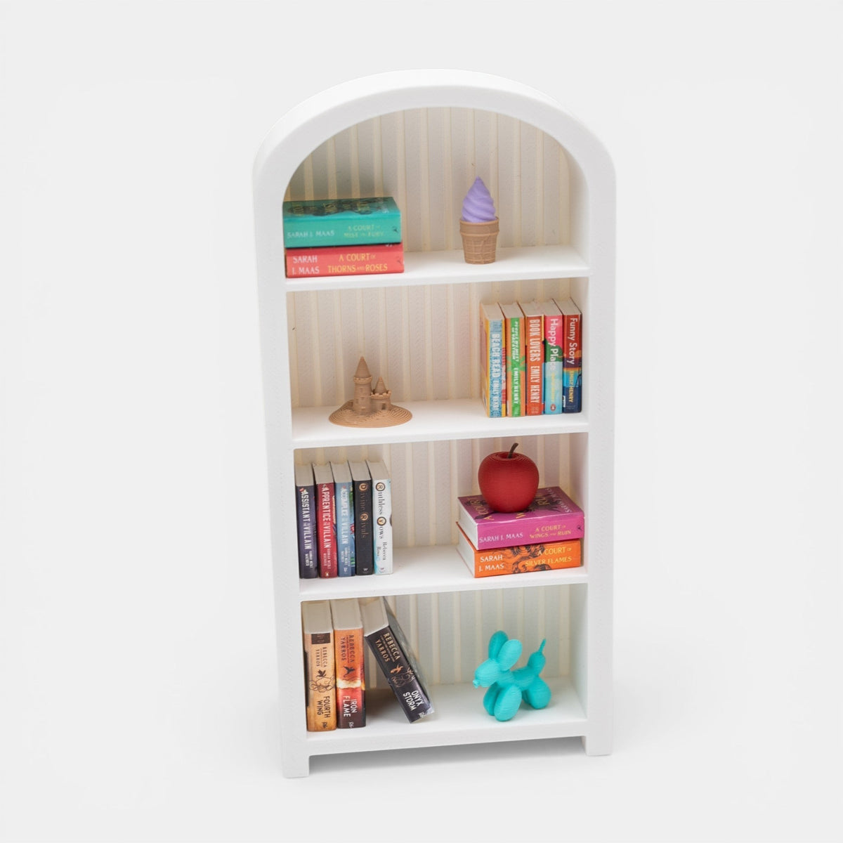 The Salty Cat Co white arched mini bookshelf filled with miniature books, a tiny apple, and decorative accessories.