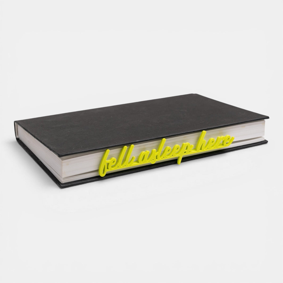 The Salty Cat Co yellow Fell Asleep Here bookmark placed on a closed black book