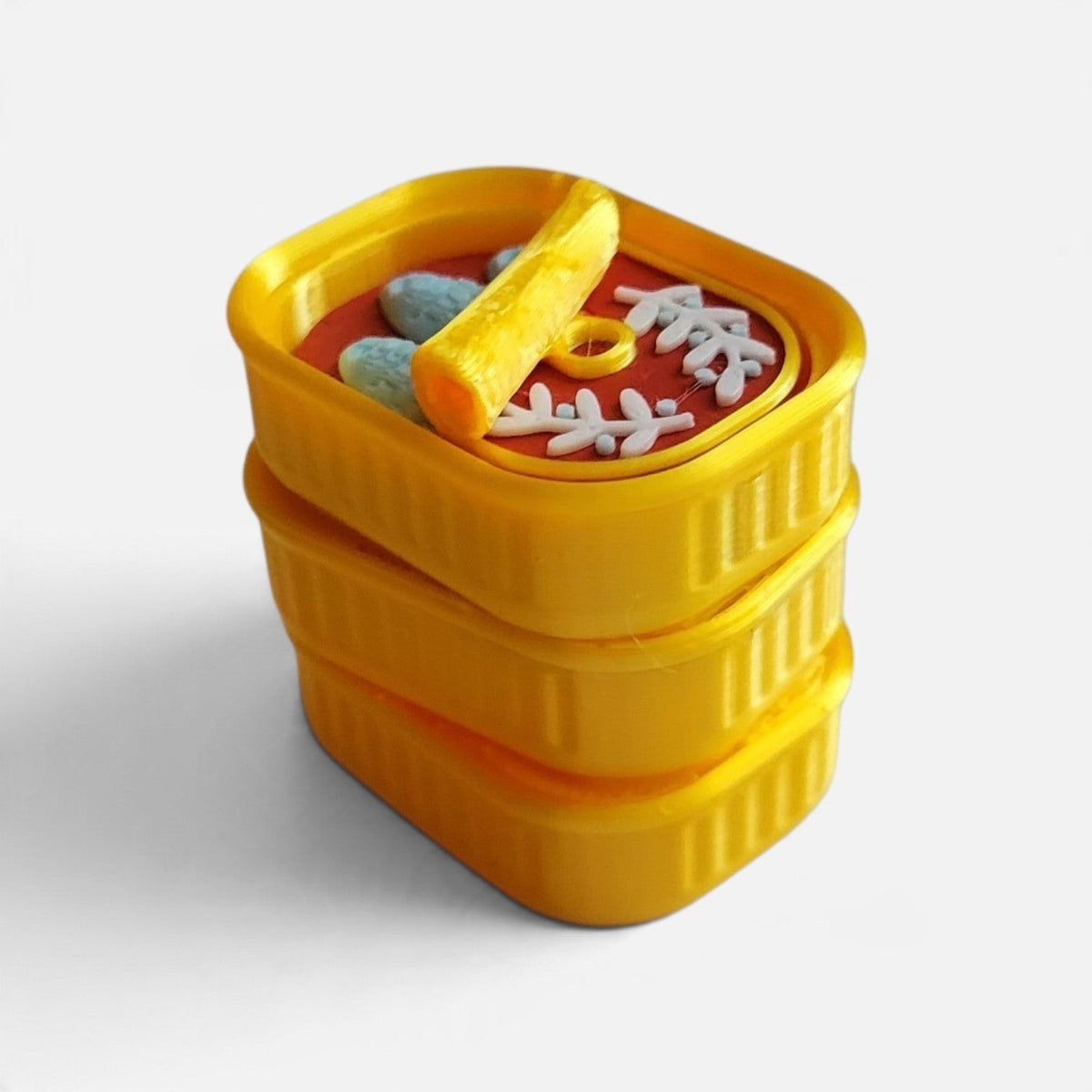 The Salty Cat Co 3D-printed yellow sardines fidget clicker toy with a red tin interior and textured fish details.